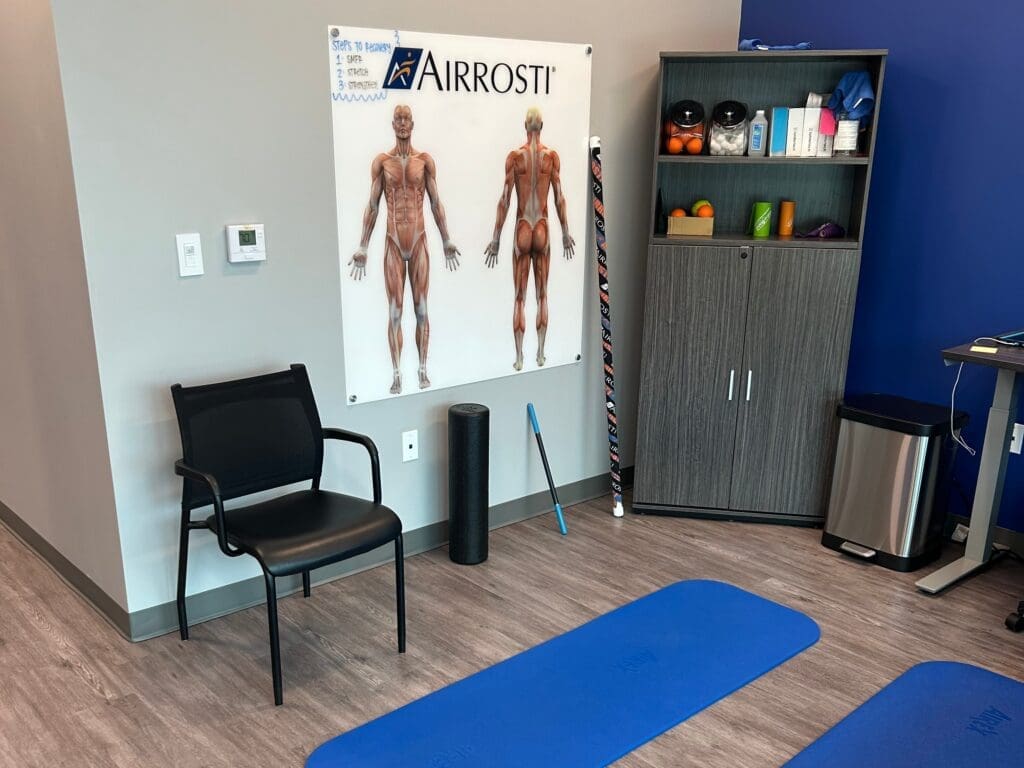 Interior view of recovery room at Airrosti Alliance. MSK diagrams posters adorn the walls. Exercise mats are laid out on the floor.