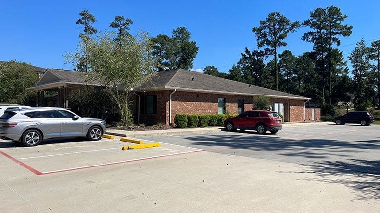 An exterior view of the Airrosti Conroe building, showing a one-story office building with red brick and a brown roof.