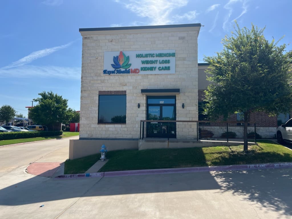 An exterior photo of the building Airrosti Murphy is located in. Excel Health MD's logo is pictured above the doors and Airrosti's logo is signed on the door.