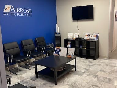 interior photo of the lobby at Airrosit Pearland. Inlcudes and Airrosti logo on the back wall and several chairs for patients to sit.