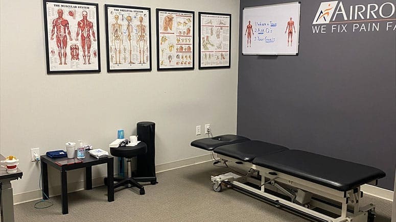 Photo of the treatment room inside Airrosti Pearland. MSK diagrams decorate the walls. Treatment table is visible.