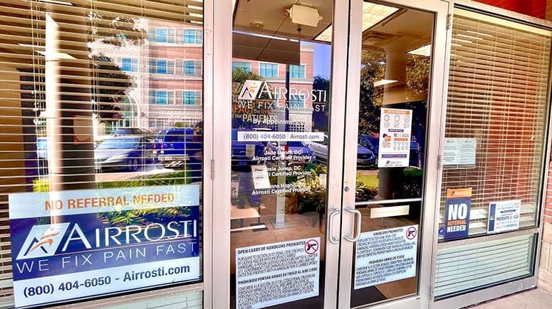 Photo of the exterior front doors at Airrosti Sugar Land. The airrosti logo and provider info are printed on the glass panes.