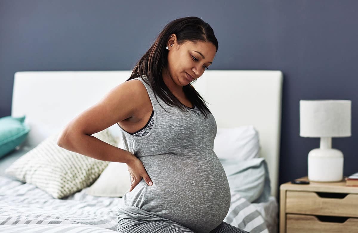 Pregnant woman getting out of bed holding her back in pain
