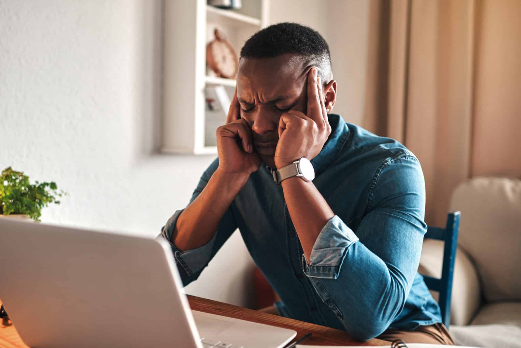 Guy at a desk next to a laptop holding his head.